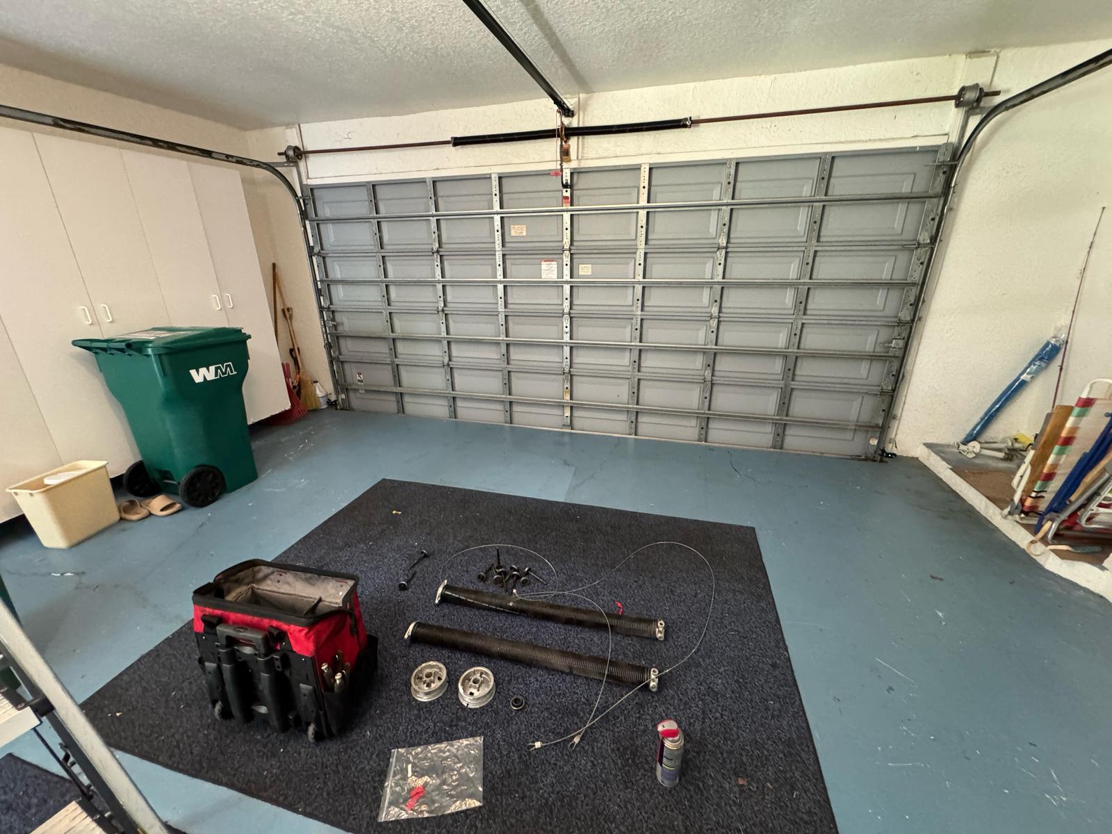 Garage door cables, drums and parts laid out on the garage floor
